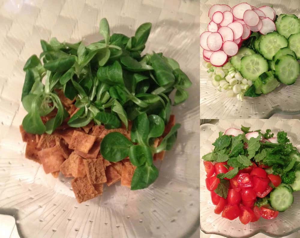 Fattoush salad preparation with toasted pita bread and lamb's lettuce in a large bowl, accompanied by sliced radishes, cucumbers, green onions, cherry tomatoes, fresh mint, and parsley ready to be mixed