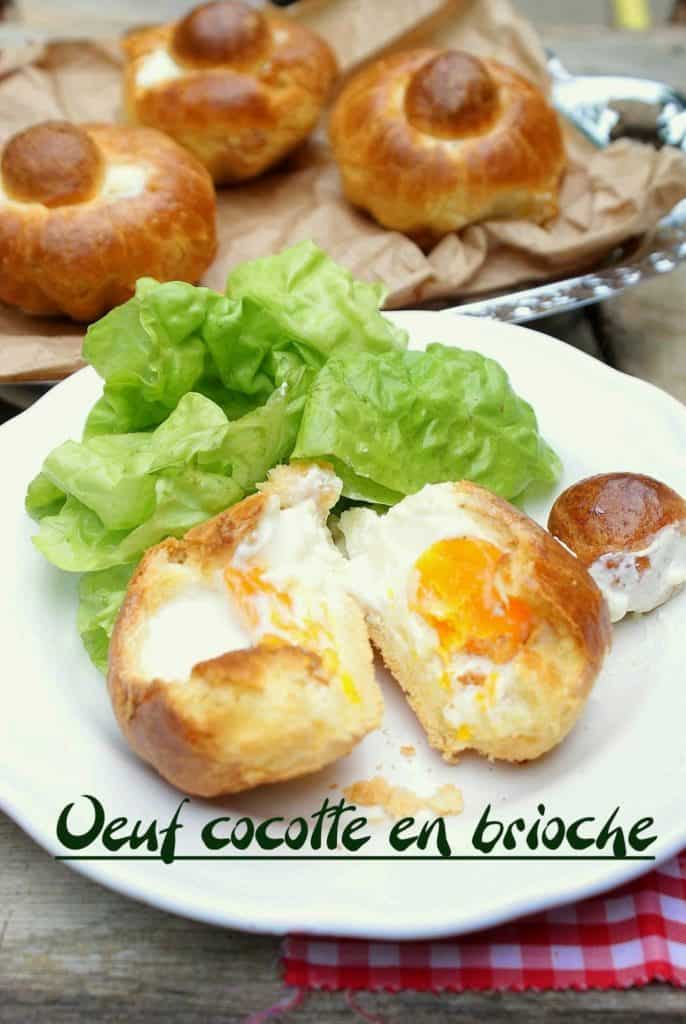 Baked egg cocotte served inside a soft brioche bun, cut open to reveal a runny yolk, plated with fresh green lettuce on a white dish. Additional whole brioche buns are visible in the background on a tray lined with parchment paper