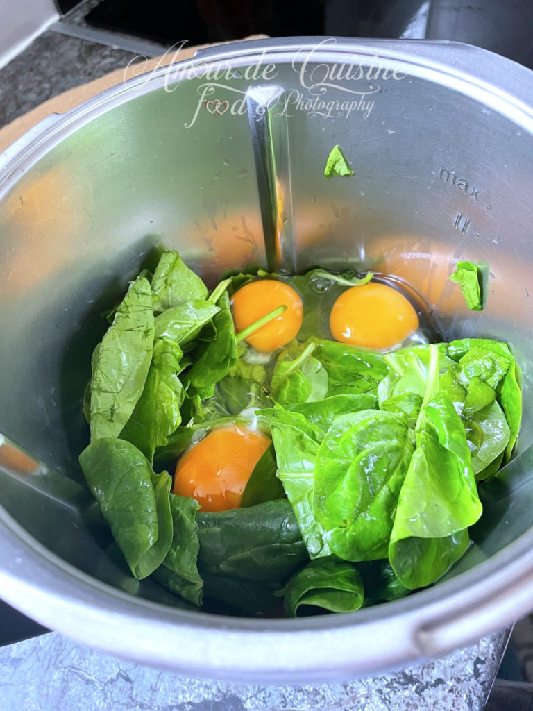 Fresh spinach leaves and raw eggs placed in a stainless steel blender bowl, ready to be mixed into a vibrant, healthy batter for gluten-free spinach tortillas