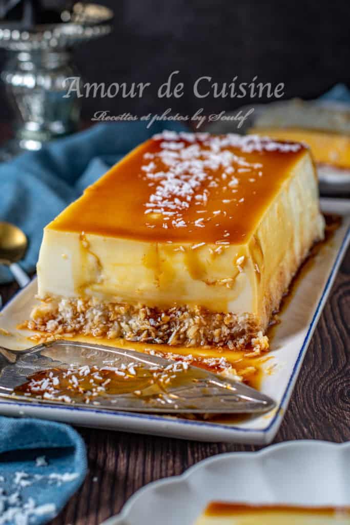 A rich french Antilles coconut flan (Flan Coco Antillais) topped with golden caramel and a sprinkle of shredded coconut, served on a rectangular plate with a cake server, showcasing its creamy custard layer and toasted coconut base