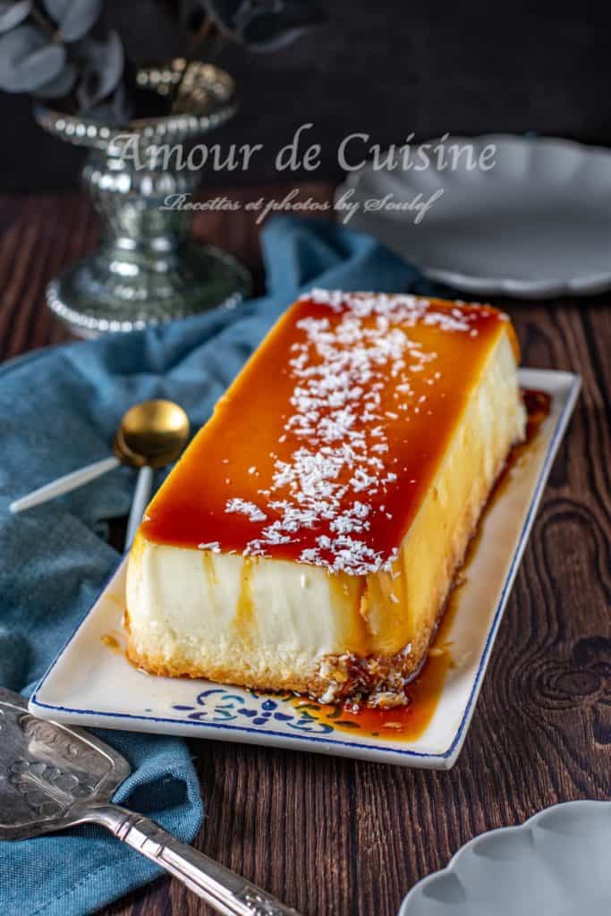 A beautifully presented Caribbean coconut flan (Flan Coco Antillais) on a rectangular plate, topped with glossy caramel sauce and a sprinkle of shredded coconut, surrounded by elegant tableware on a rustic wooden surface