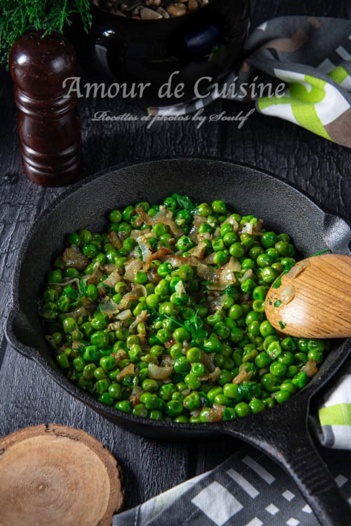 Butter-sautéed green peas with onions and parsley served in a black cast iron skillet, with a wooden spoon resting on the side, styled on a dark rustic table