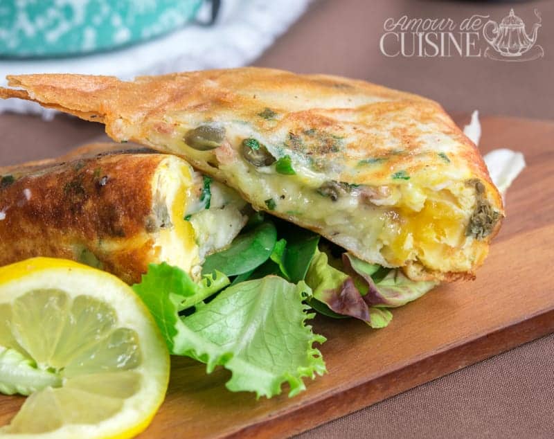 Crispy Tunisian brik filled with egg, tuna, capers, and herbs, served on a bed of fresh salad with a slice of lemon.