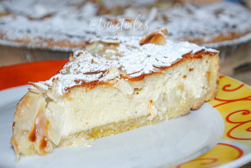 Close-up of a slice of pear amandine tart with creamy almond filling, flaked almonds, and powdered sugar on top, served on a decorative yellow and red plate
