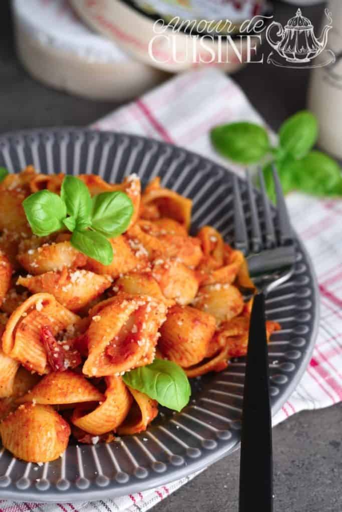 Plate of shell pasta in tomato sauce, topped with grated parmesan and fresh basil leaves, served on a grey plate with a fork