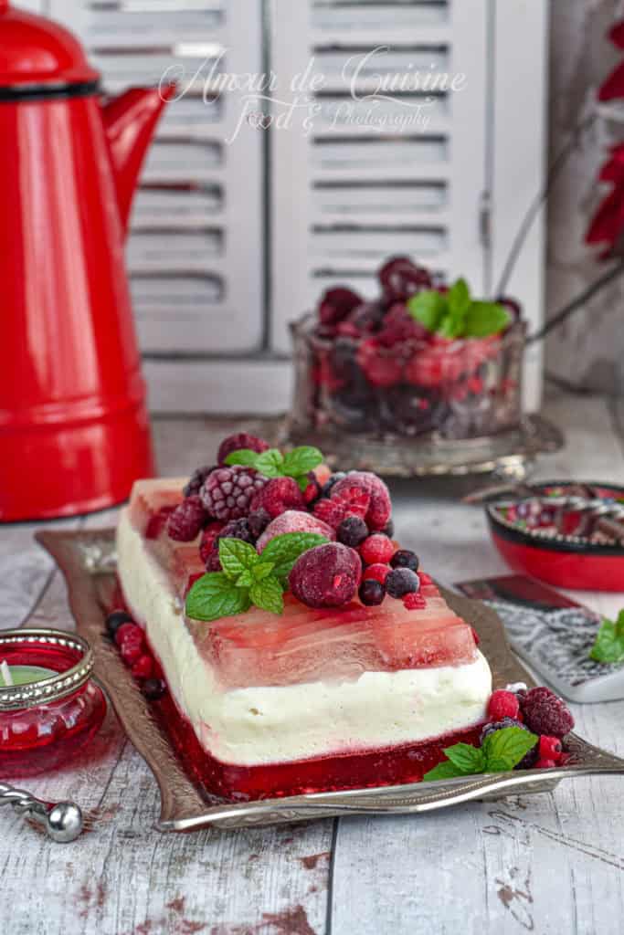 Layered panna cotta terrine with vanilla and red fruit jelly, topped with frozen berries and fresh mint, presented on a silver tray with vintage red and white kitchen decor