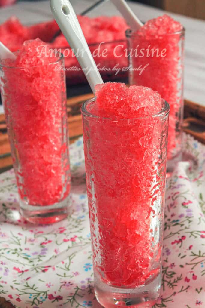 Tall glasses filled with bright red grenadine granita topped with ceramic spoons, placed on a floral-patterned cloth—refreshing homemade frozen dessert made with pomegranate syrup