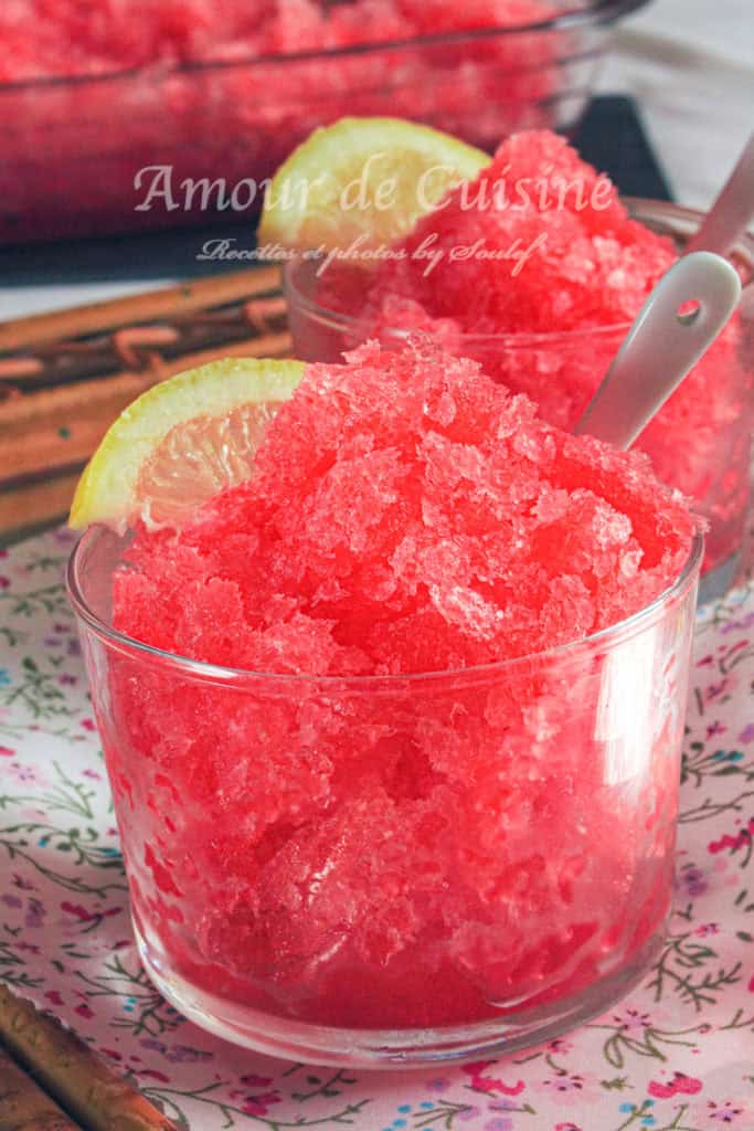 Glass bowl filled with vibrant red grenadine granita, garnished with a lemon slice and served with a spoon—refreshing homemade frozen dessert made with pomegranate syrup, perfect for summer.